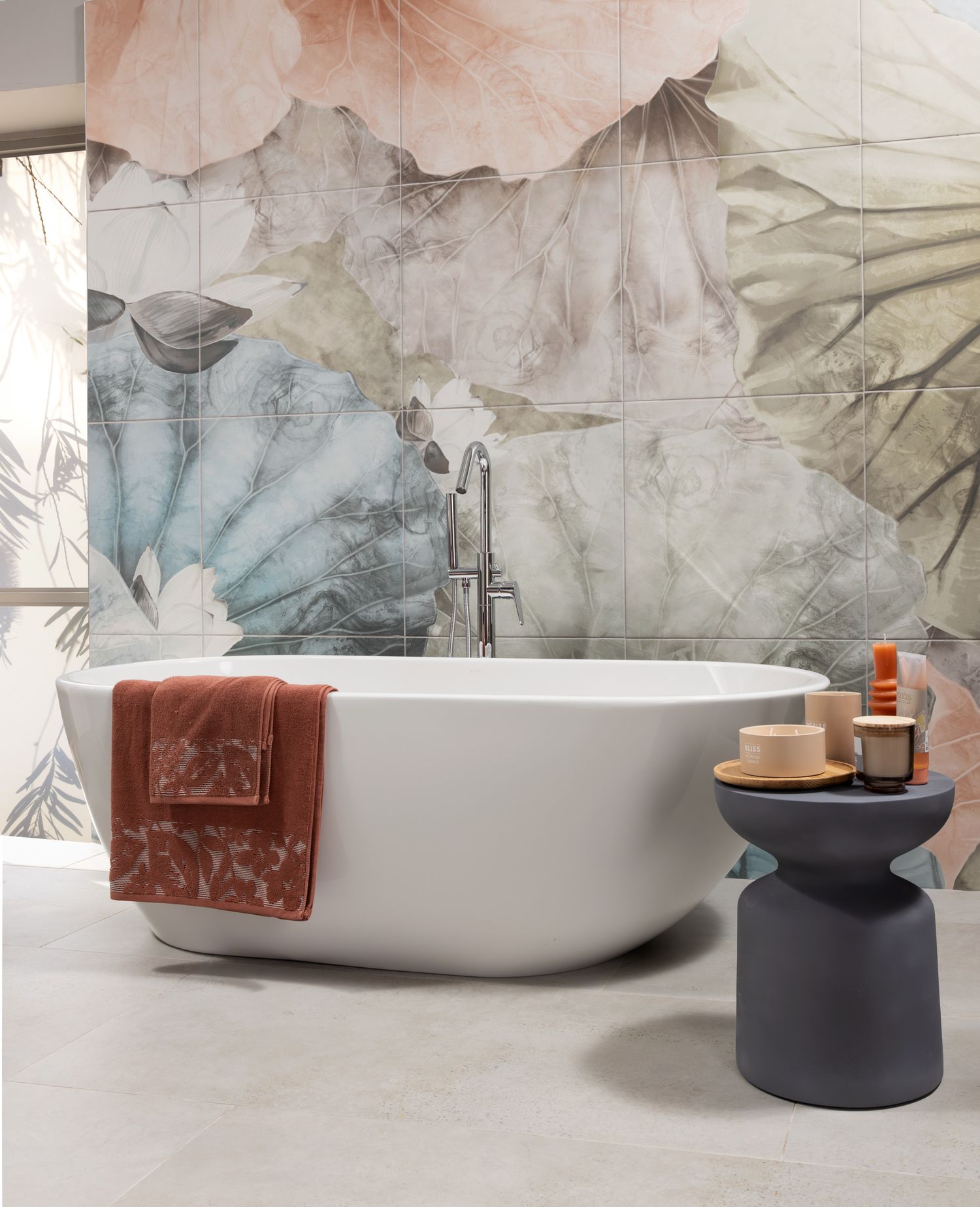 Modern freestanding white bathtub against watercolor-style wallpaper with decorative side table.