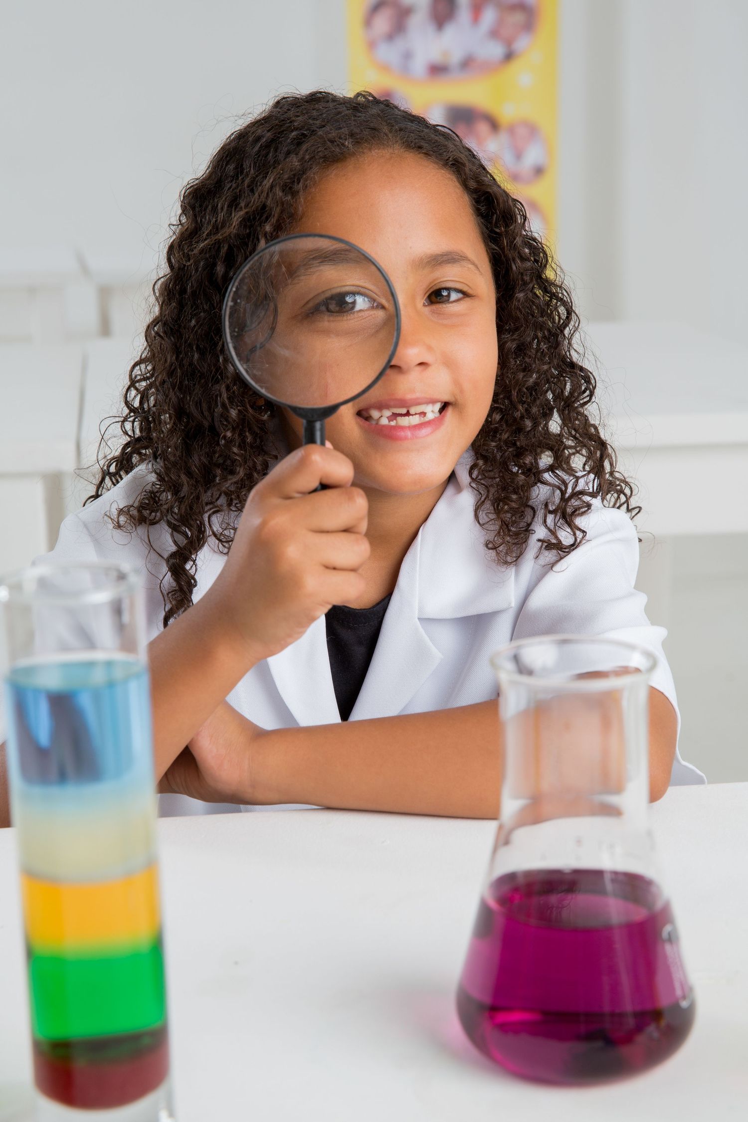Young scientist examines colorful liquids through a magnifying glass during a science experiment.