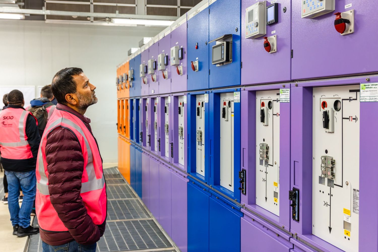 Visitor observing colorful control panels and electrical equipment in a technical facility.