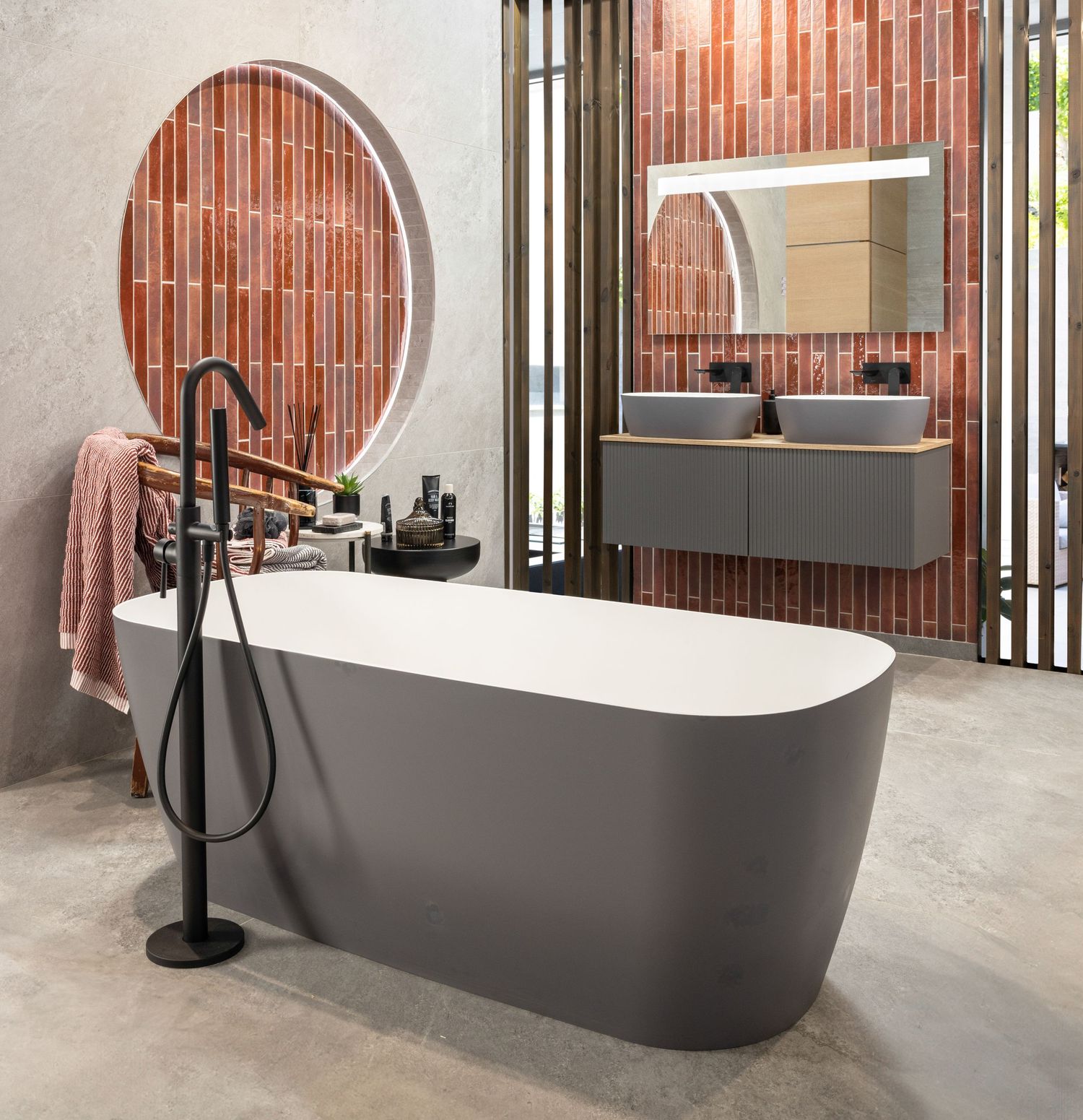 Sleek dark freestanding bathtub positioned near wooden slatted windows in a minimalist bathroom setting.