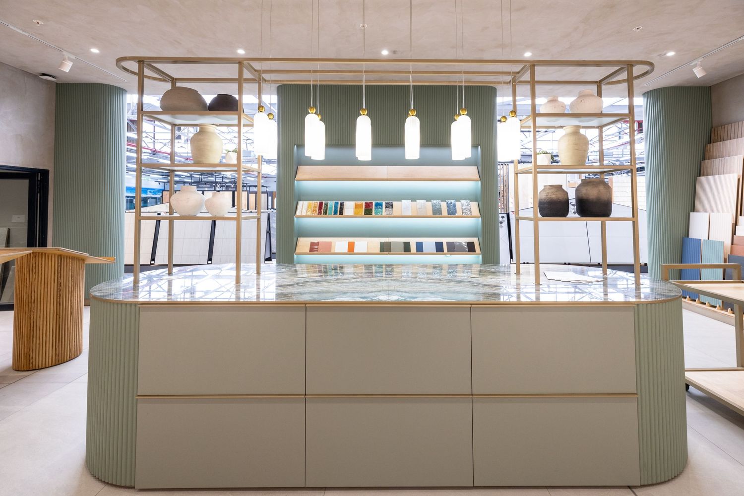 Long retail counter with sage green base cabinets and white countertop in a modern showroom setting.