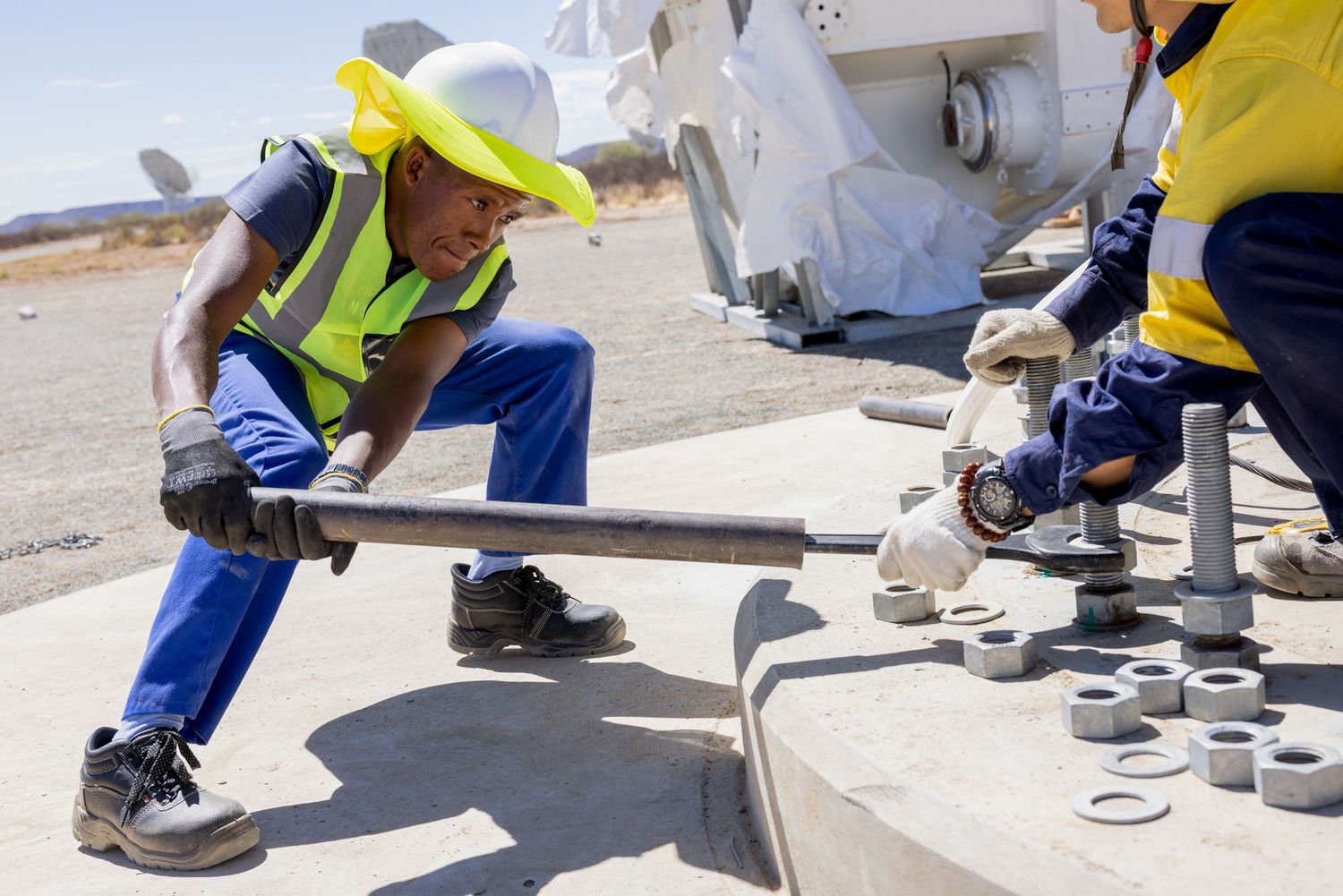 Construction worker in protective gear measures grout thickness between concrete pavers during installation process.