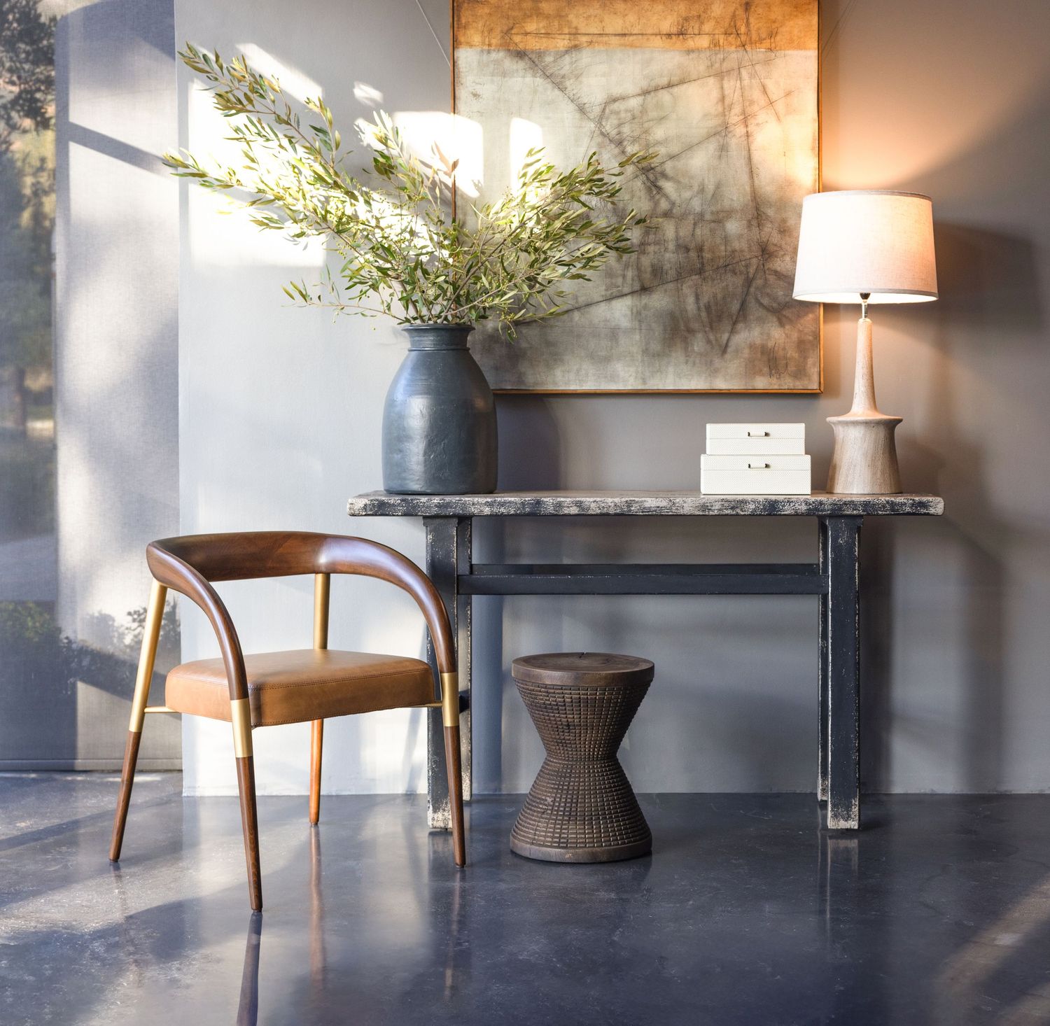 Modern interior design featuring a wooden chair, console table and vase with greenery in natural sunlight.