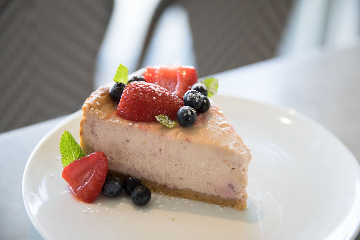 A slice of pink cheesecake topped with fresh strawberries and blueberries on a white plate.
