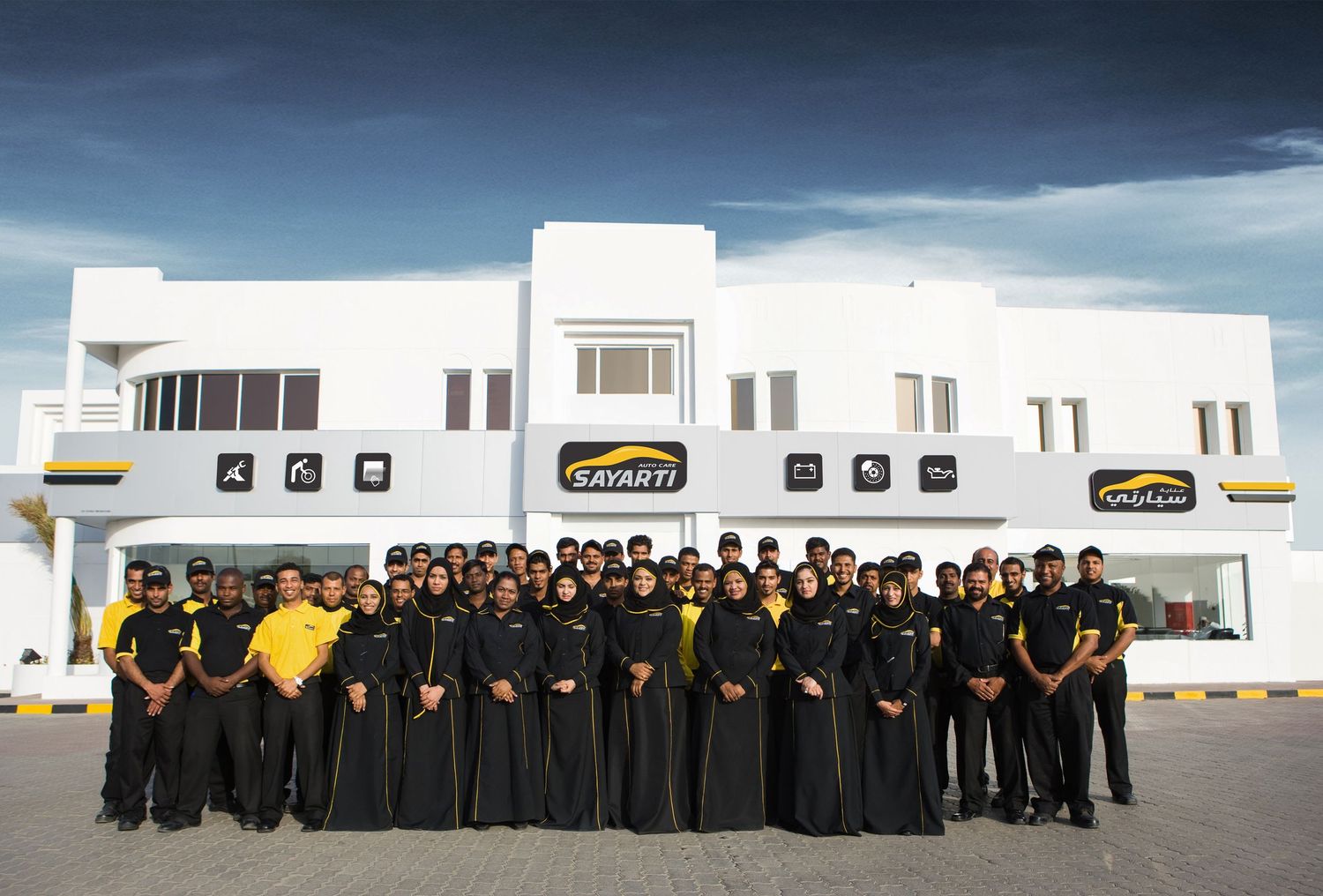 Large group of automotive service professionals lined up outside modern white facility.