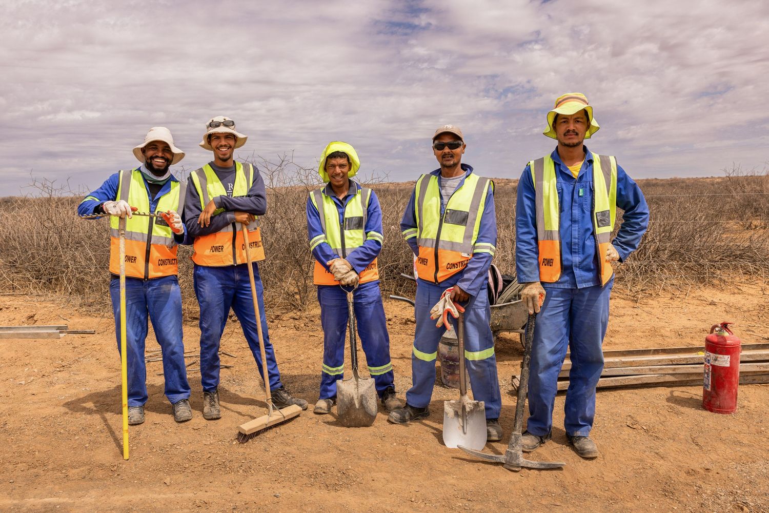 Workers with tools and equipment pose together at desert construction site.