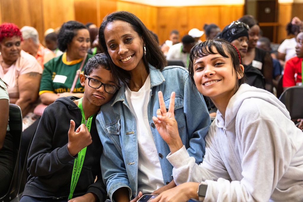 Students sitting together in a crowded auditorium smile and engage with each other during a school event.