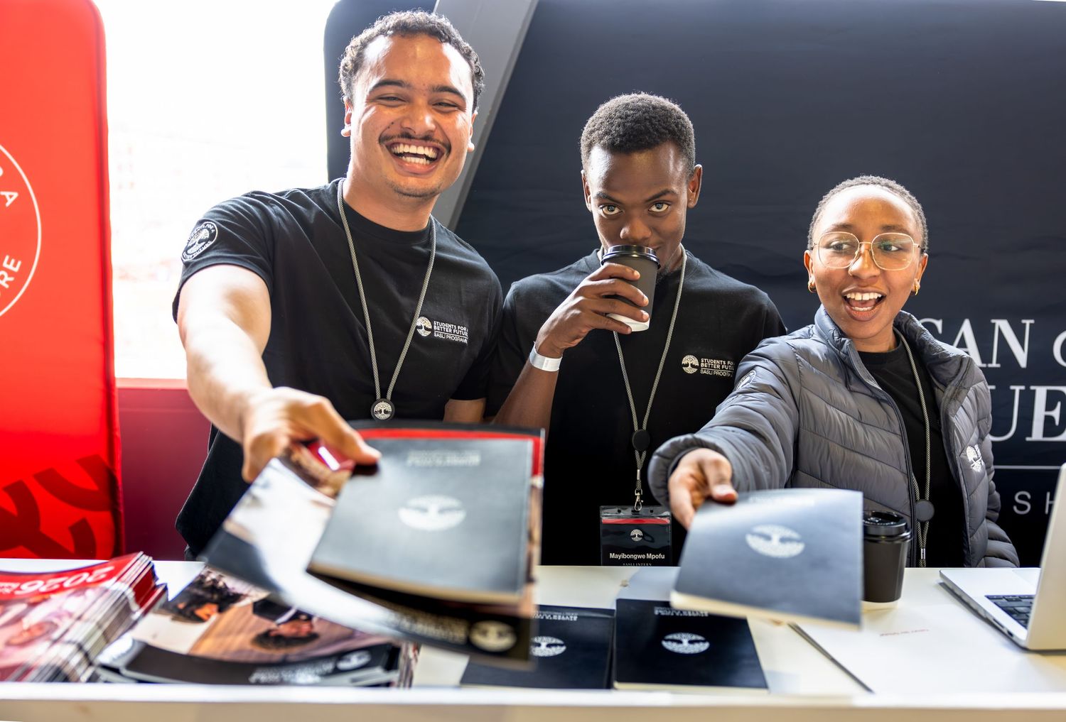 Staff members interact enthusiastically while working at an event registration desk.