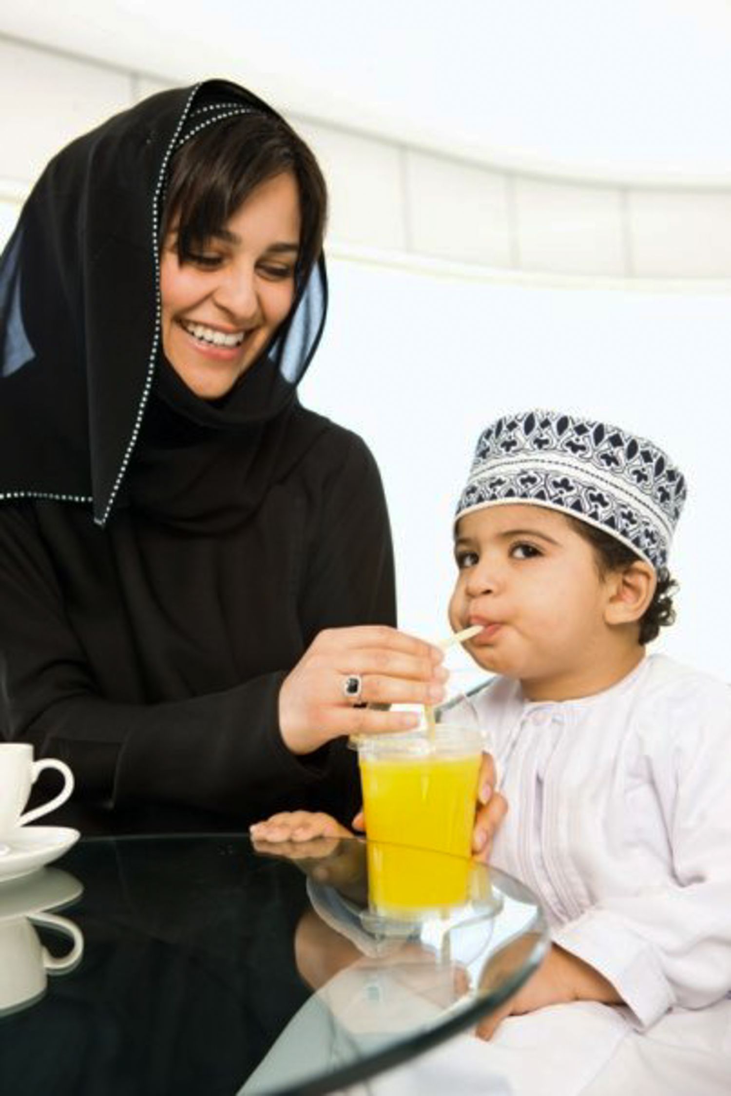 A series of progressive photos showing someone helping a child drink orange juice while wearing traditional Islamic attire.
