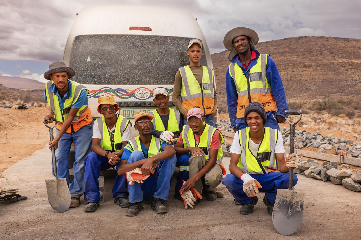 Construction team members with tools and equipment gather at desert worksite.