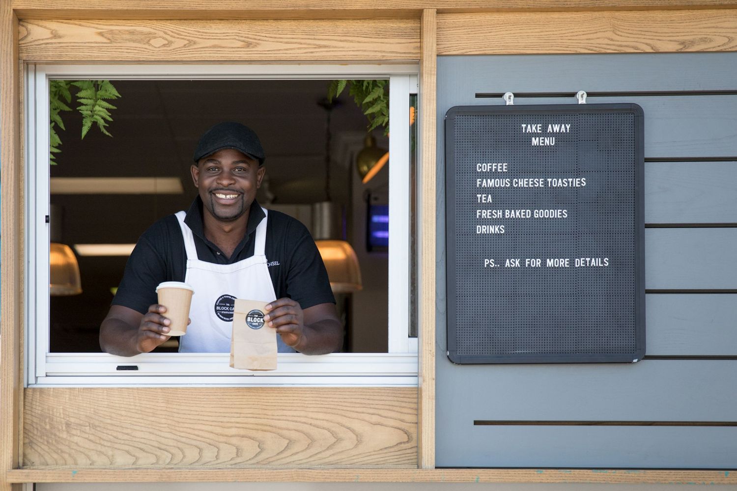 A friendly barista serving coffee through a wooden service window.