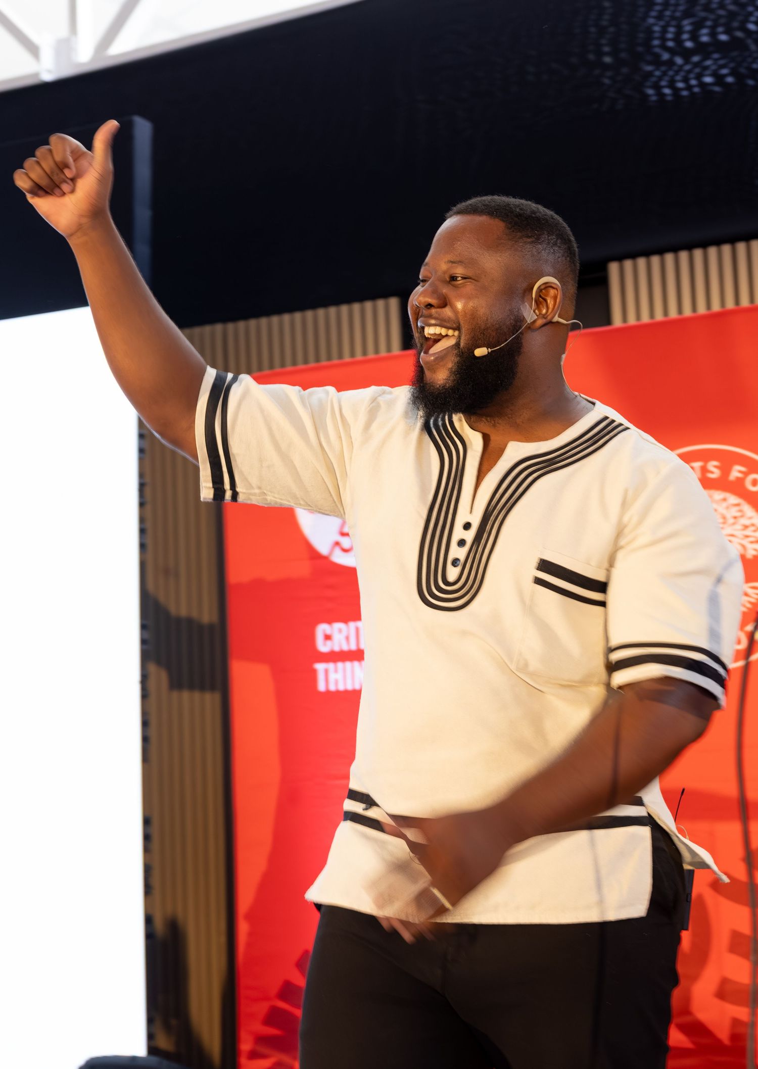 A person in a cream-colored traditional African shirt raises their fist in celebration on stage.