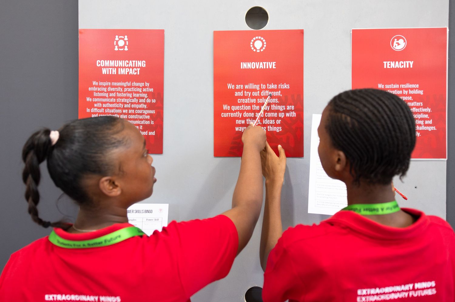 Students in red uniforms read information posted on coral-colored wall signs.