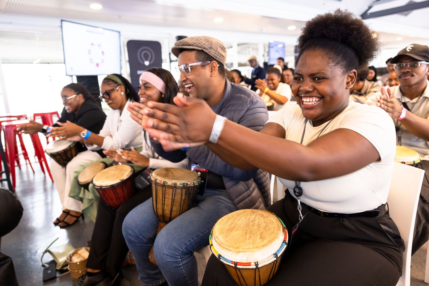 A group of people play drums together during an interactive team building workshop.