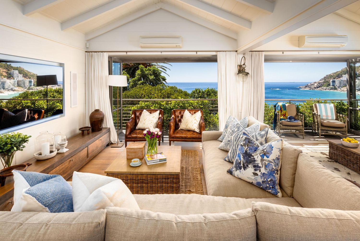 Luxury beachfront villa interior with white decor and panoramic ocean views through floor-to-ceiling windows.