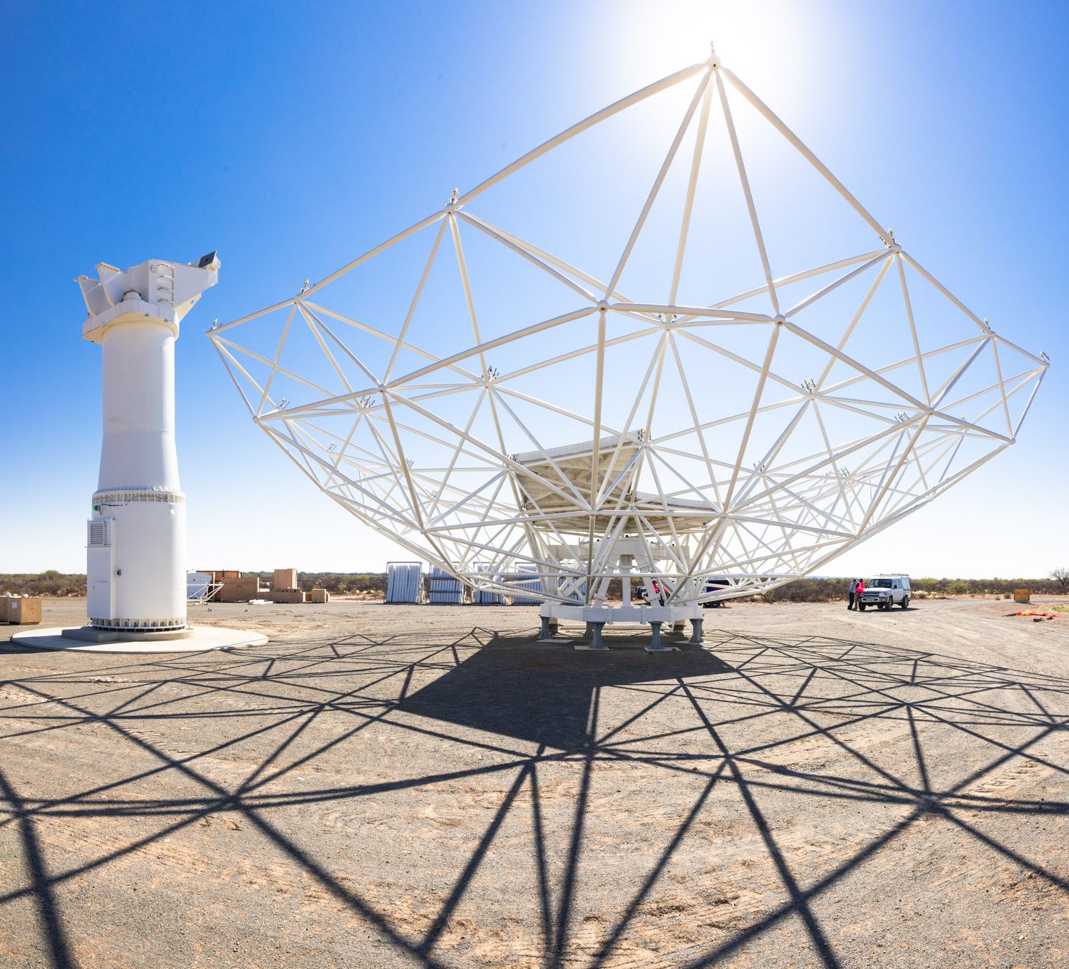 Large metal framework and antenna structures casting shadows against desert ground.