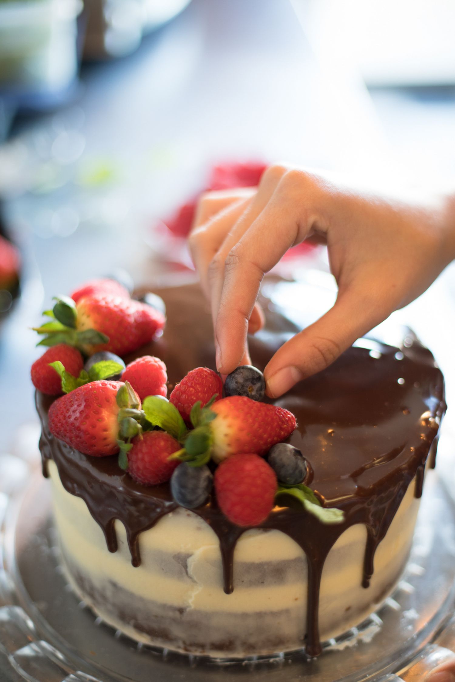 Decorating a chocolate-drizzled cheesecake with fresh strawberries and raspberries.