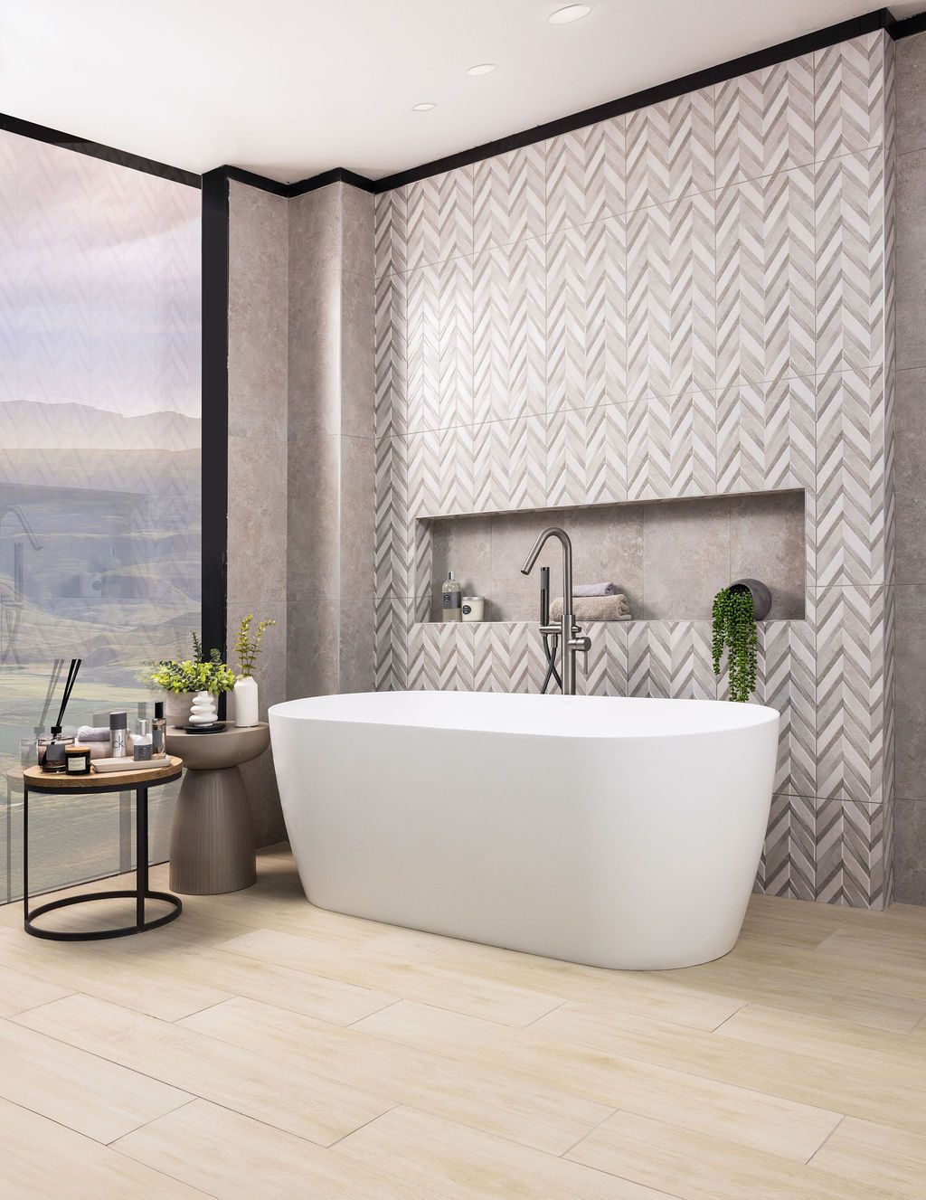Contemporary bathroom featuring chevron tile walls, freestanding white bathtub, and light wood flooring with scenic views.