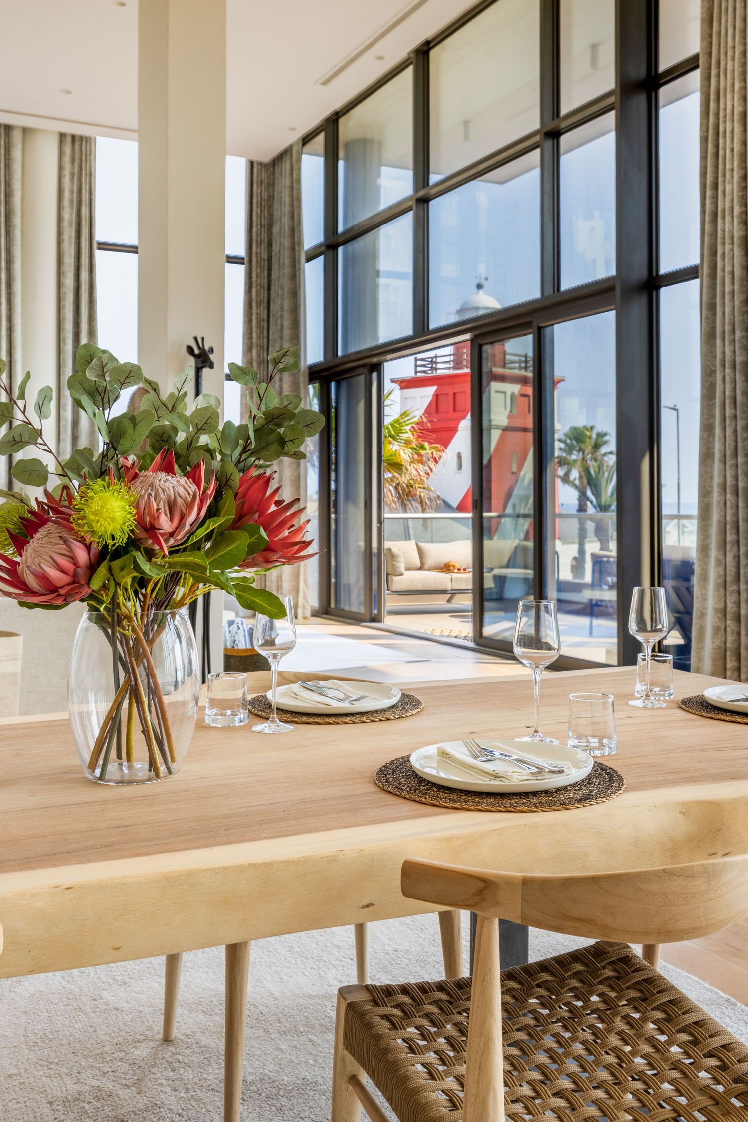 Dining area with wooden table and tropical flower arrangements near large windows with ocean views.