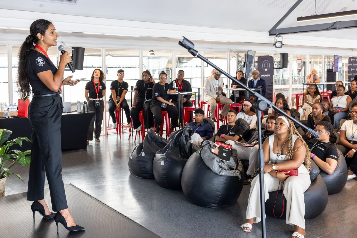 Speaker presents to an audience seated on bean bags in a modern conference space.
