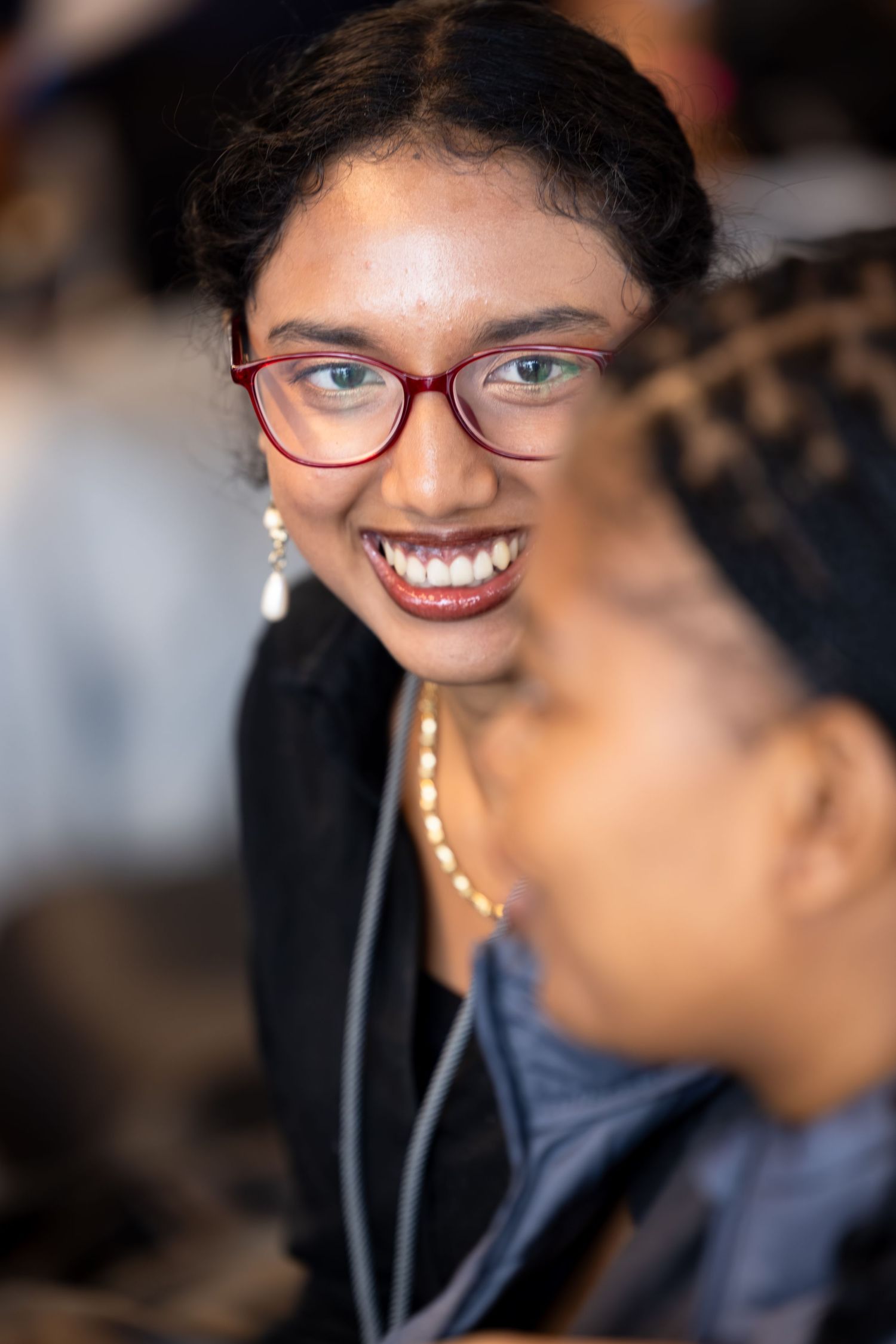A participant wearing red-framed glasses smiles during a professional event.
