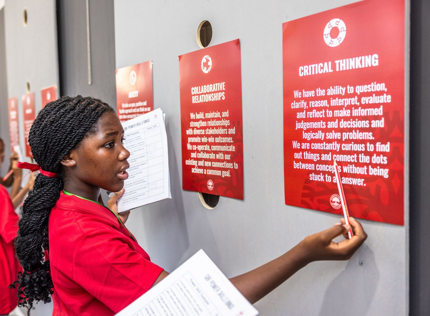 Students examine red educational posters mounted on a wall during a learning activity.