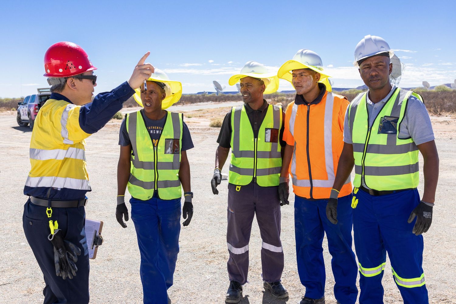 Team of workers in safety gear and hard hats discuss project at construction site.