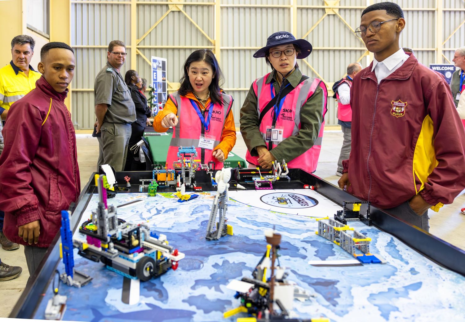 Students gather around robotics display table showcasing various mechanical projects.