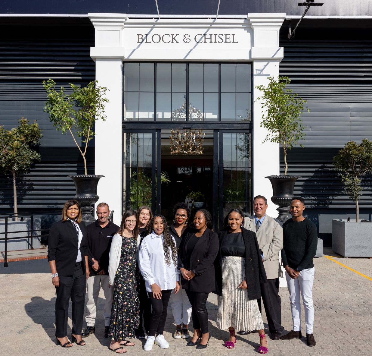 Group photo of retail staff standing outside modern Block & Chisel storefront with glass facade.