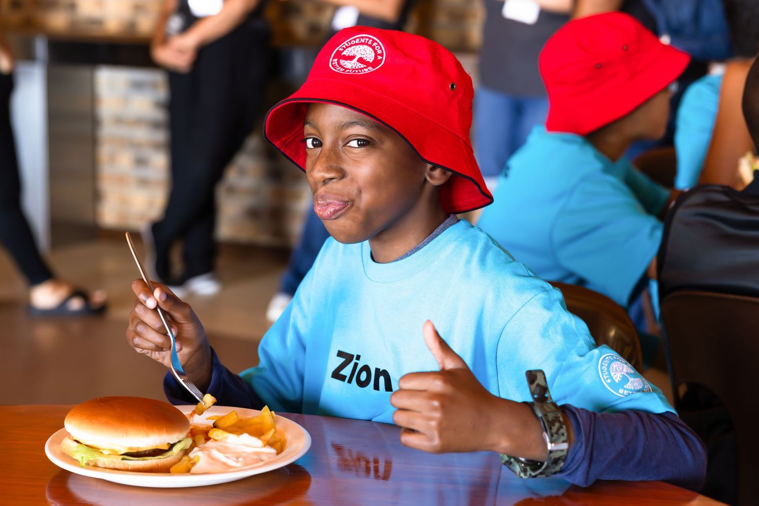 Students in blue and red caps enjoying a meal at tables.