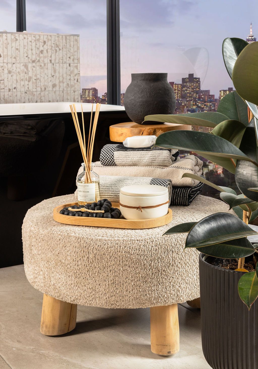 Stylish round textured ottoman with wooden legs and decorative accessories displayed in a modern living space.