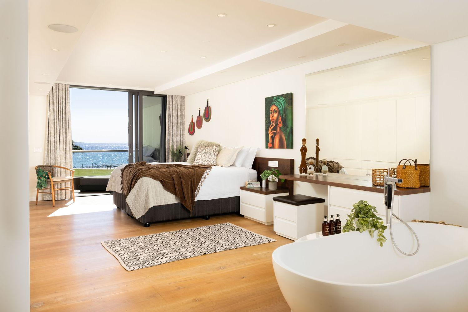 Modern minimalist living room with white walls, hardwood floors and large windows offering panoramic ocean views.