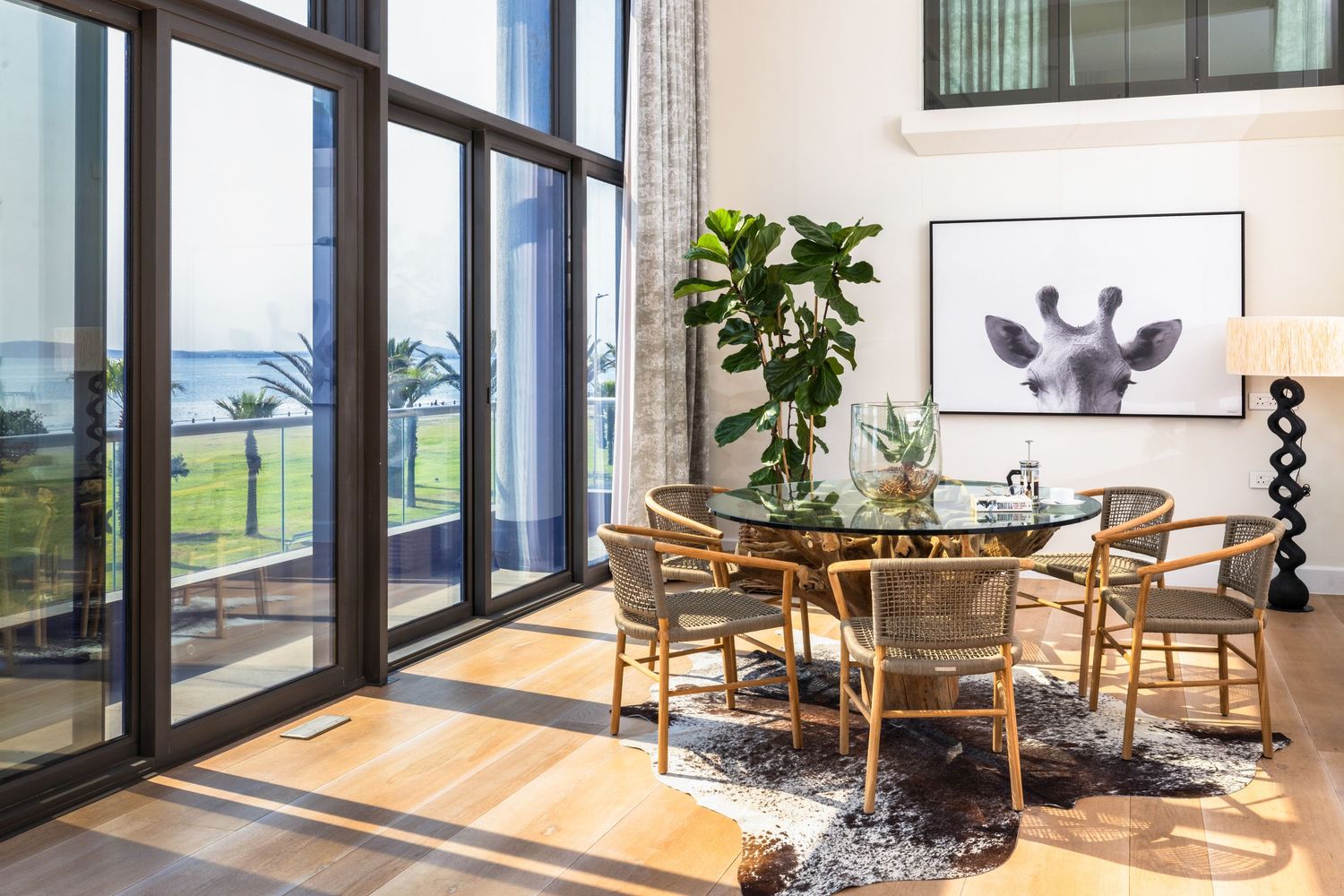 Bright dining area with wooden chairs and glass table next to large windows overlooking scenic views.