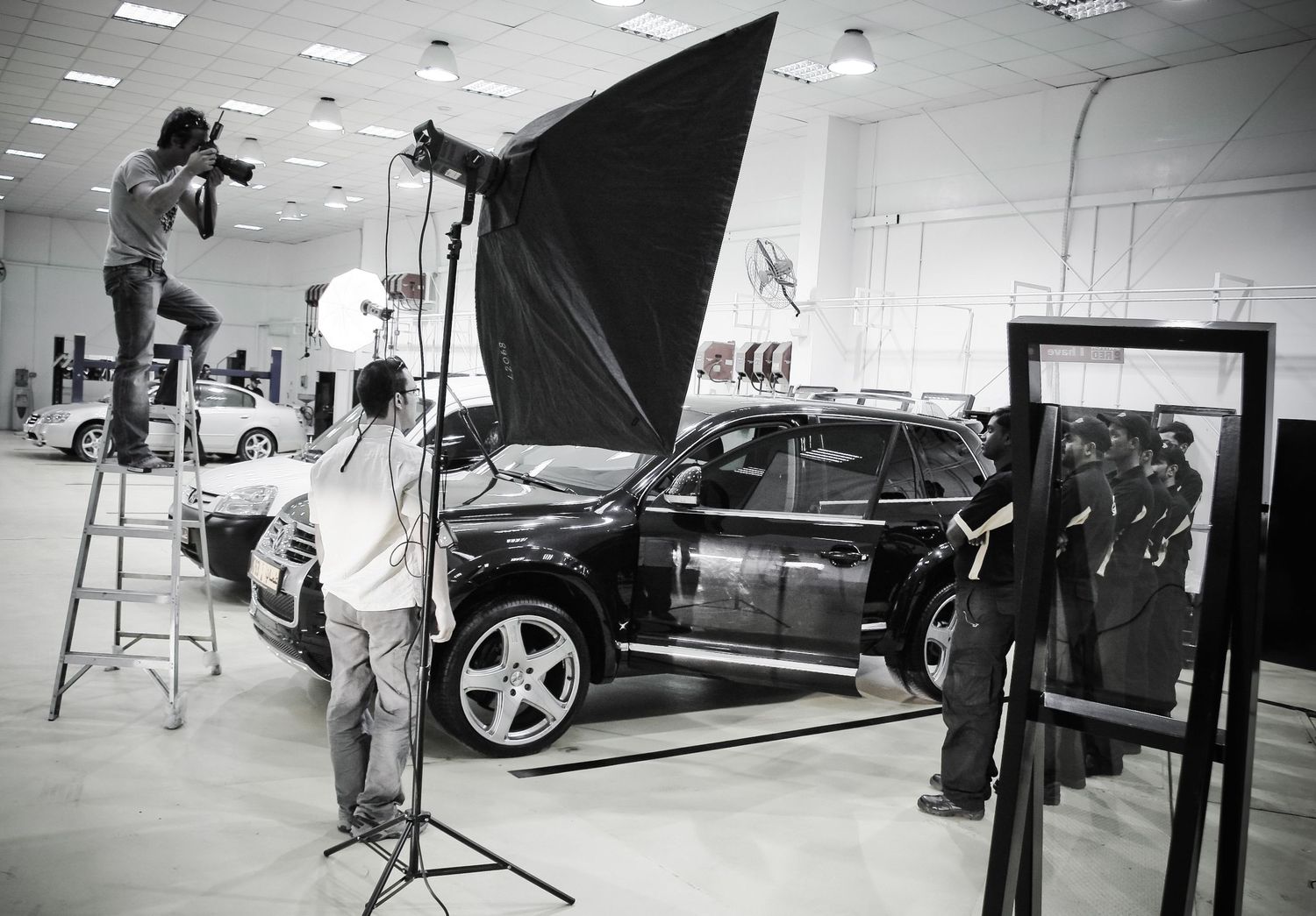 Black and white photo montage showing behind-the-scenes photography studio setup with lighting equipment and vehicles.