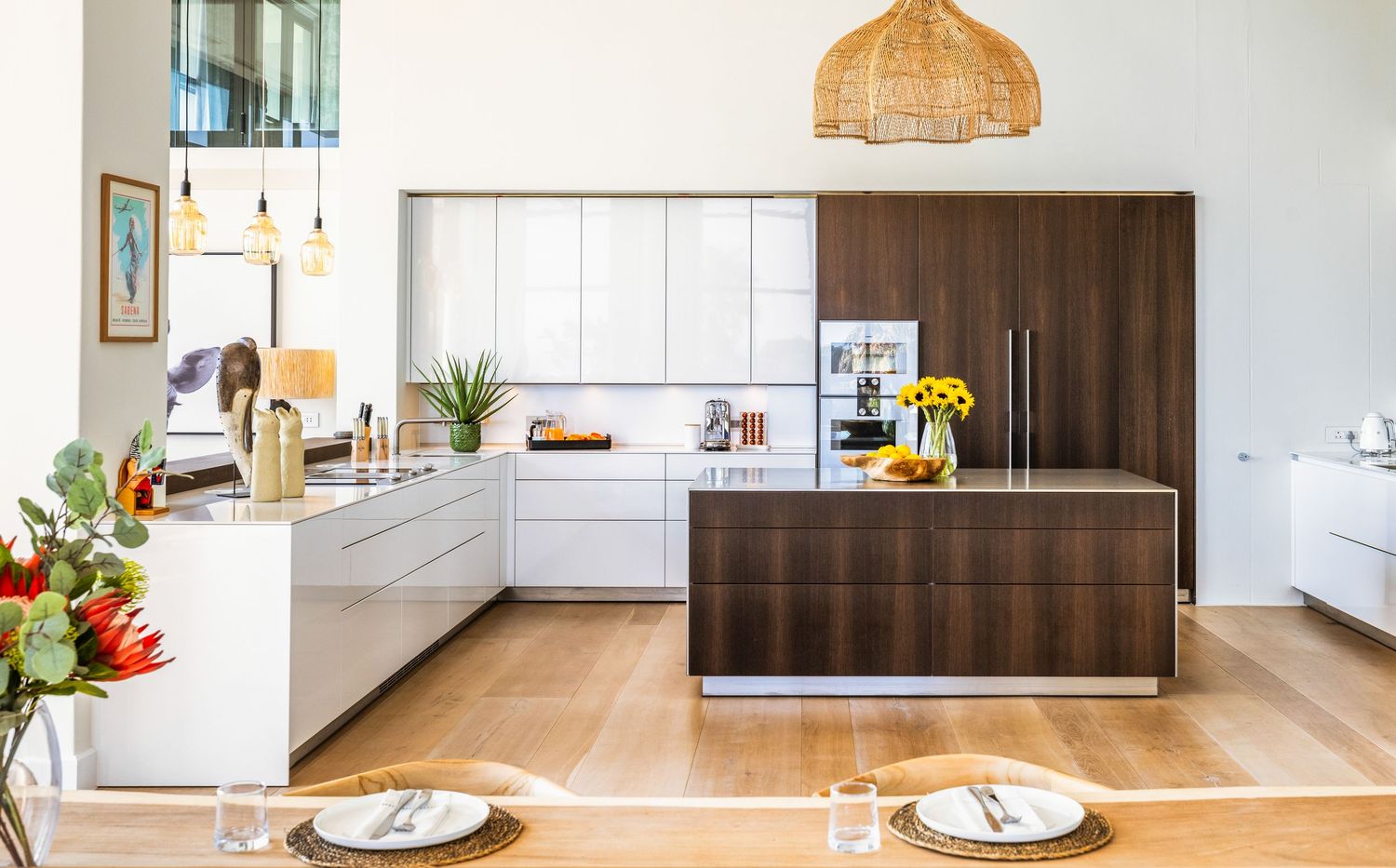 Contemporary open concept kitchen with white cabinets, dark wood accents, and minimalist design elements.