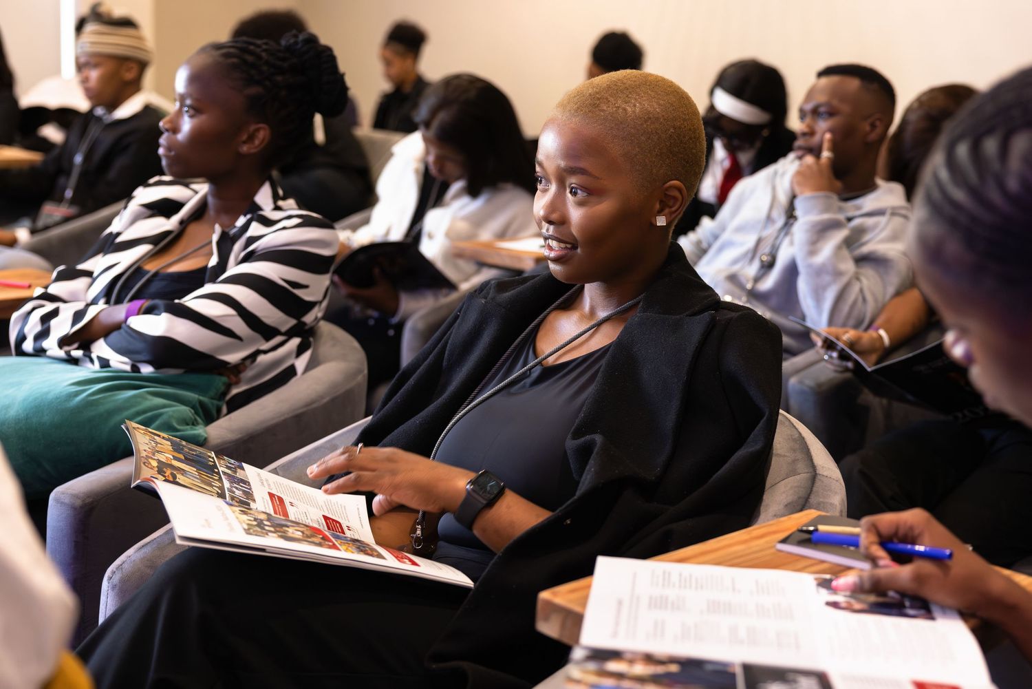 Conference attendees sit in rows taking notes during a professional presentation.