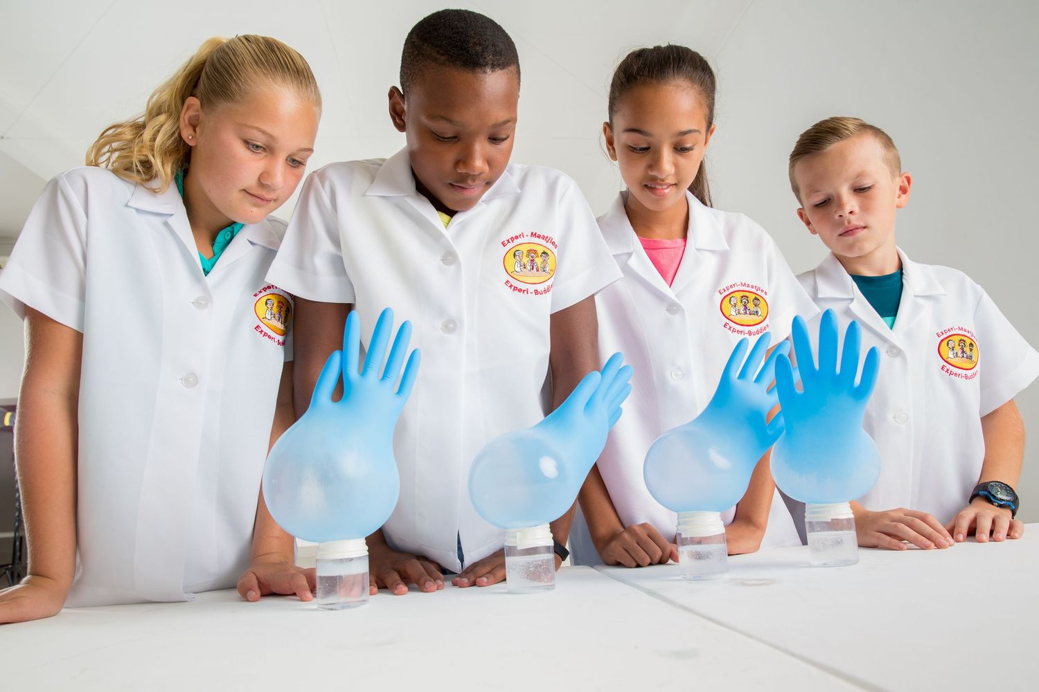 Students wearing lab coats and blue gloves look down at a science experiment together.
