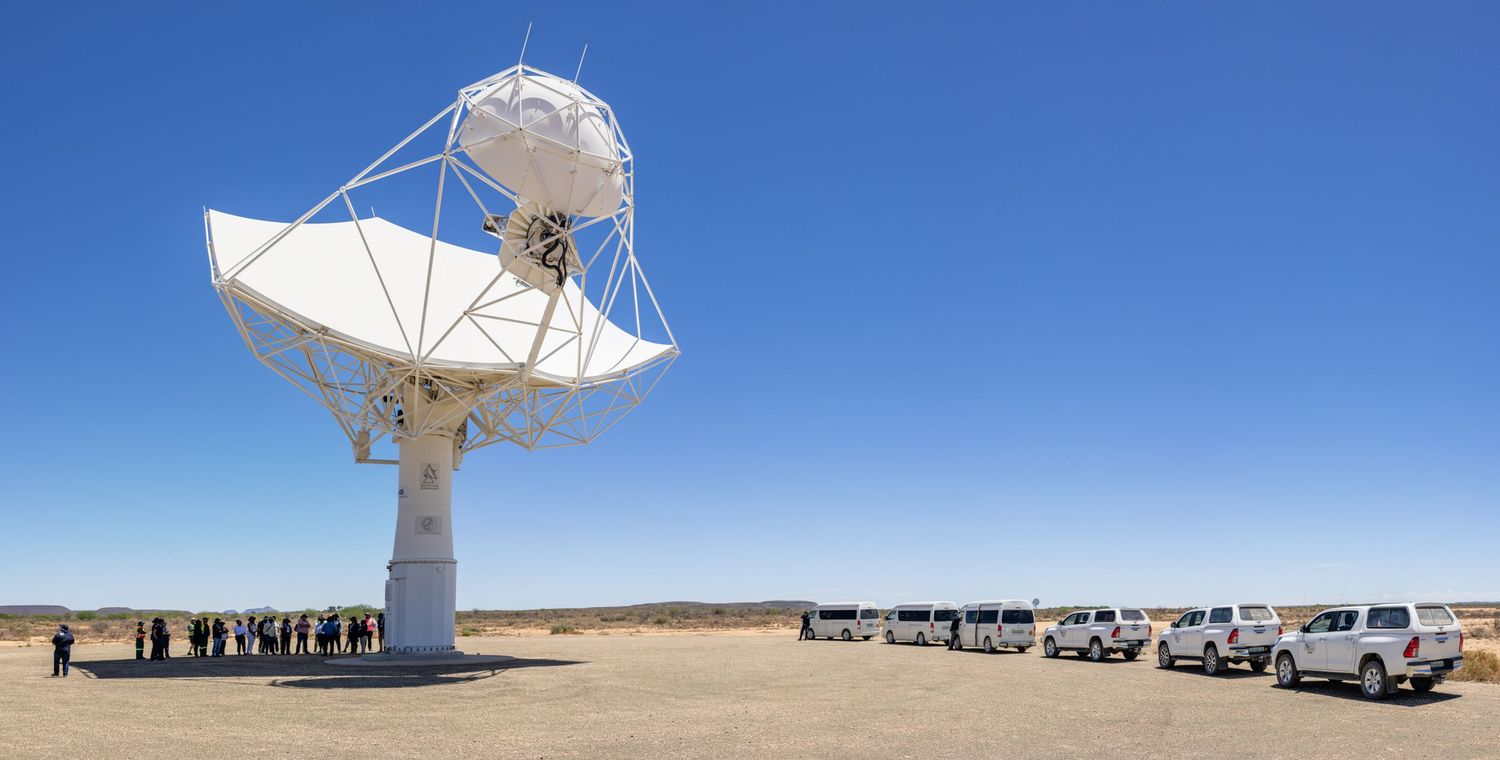 Large satellite dishes and array of vehicles in desert landscape under bright blue sky.