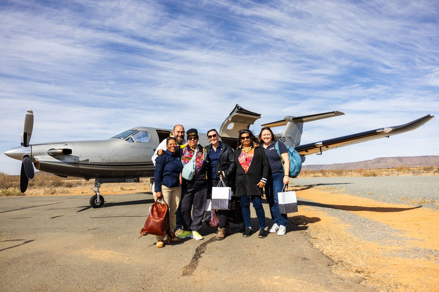 Small propeller aircraft on desert airstrip with tour group gathered nearby.