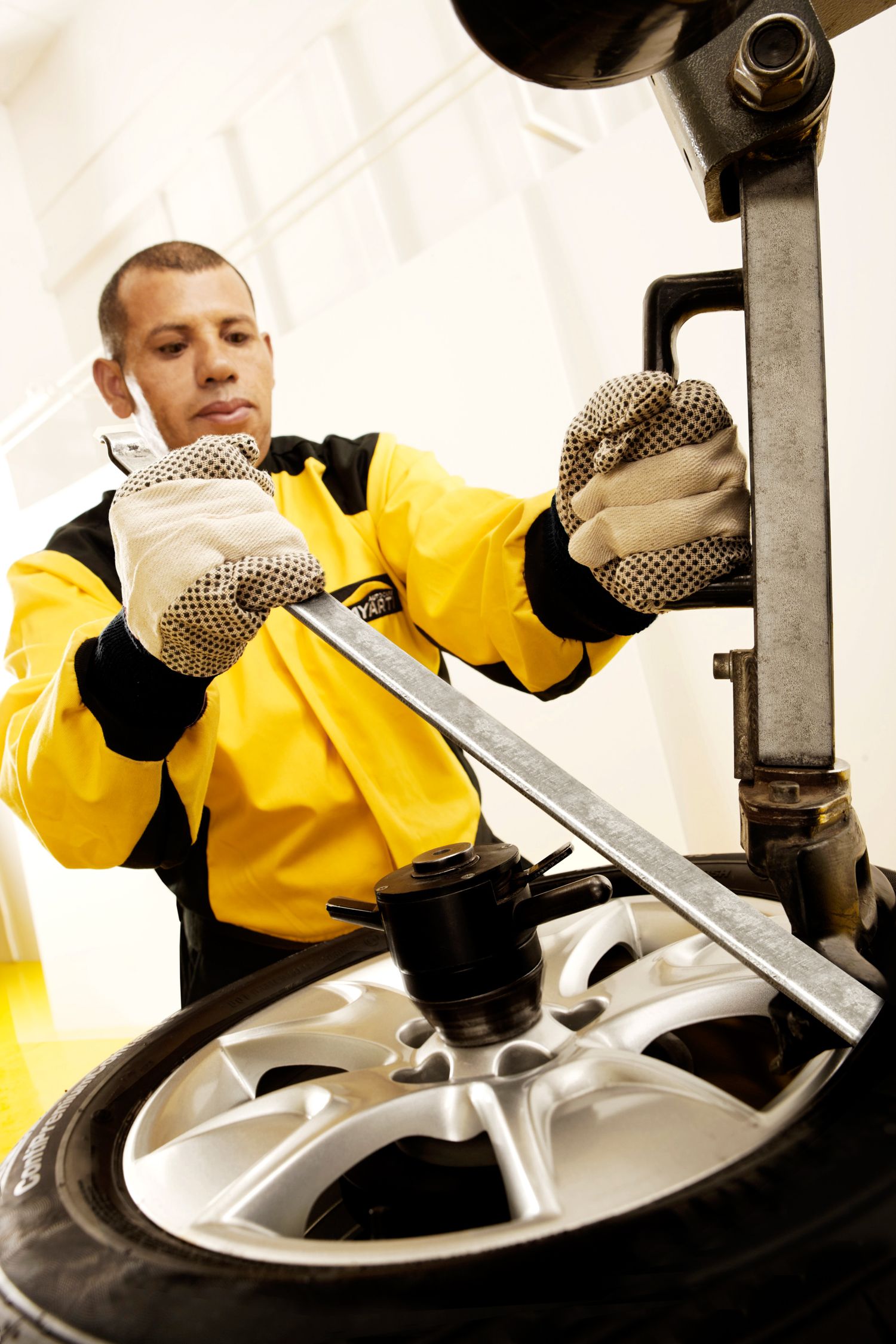 Auto mechanic in yellow safety jacket using tools to service and balance a silver alloy wheel and tire.