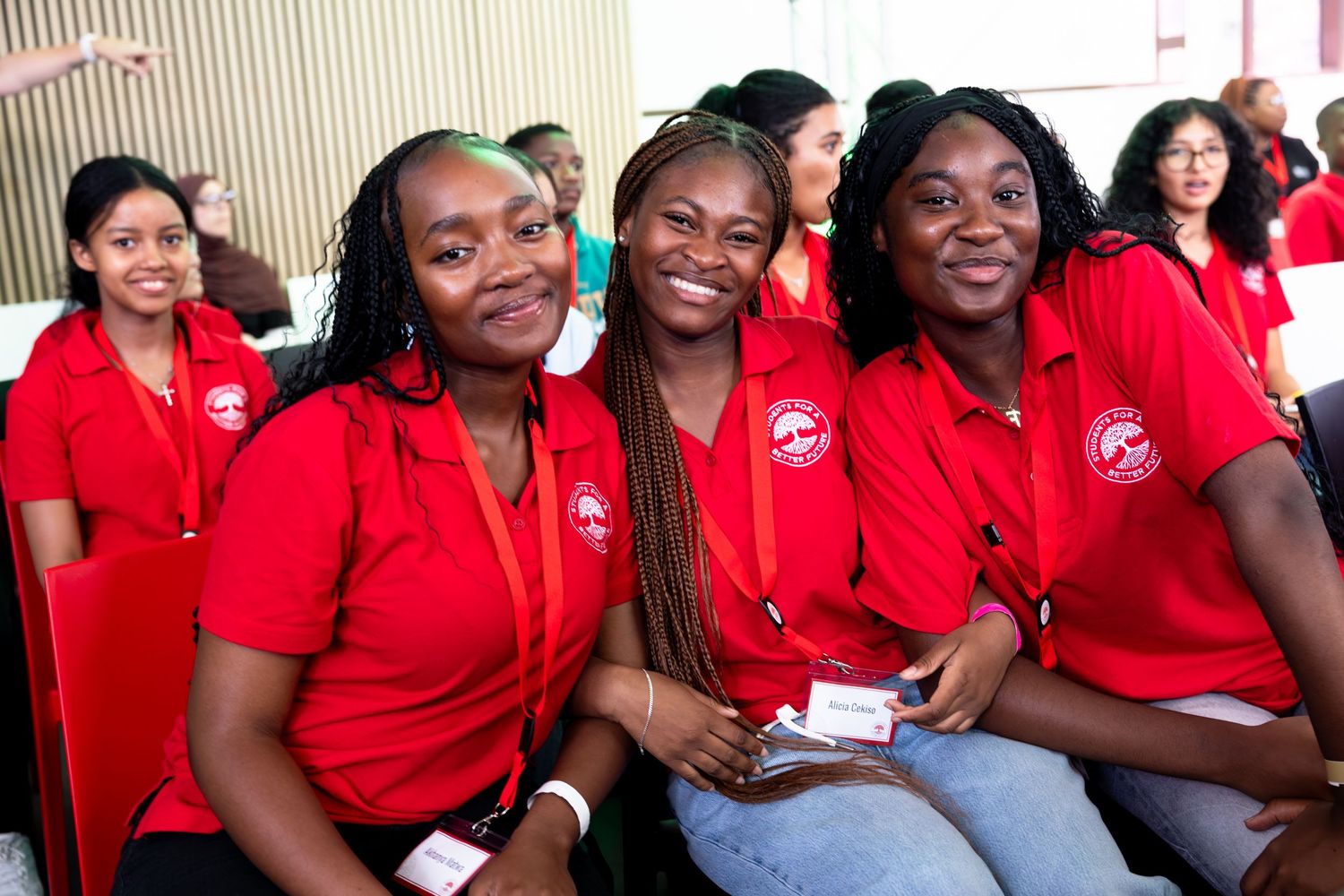 Group of students wearing matching red polo shirts gather together in a classroom setting.