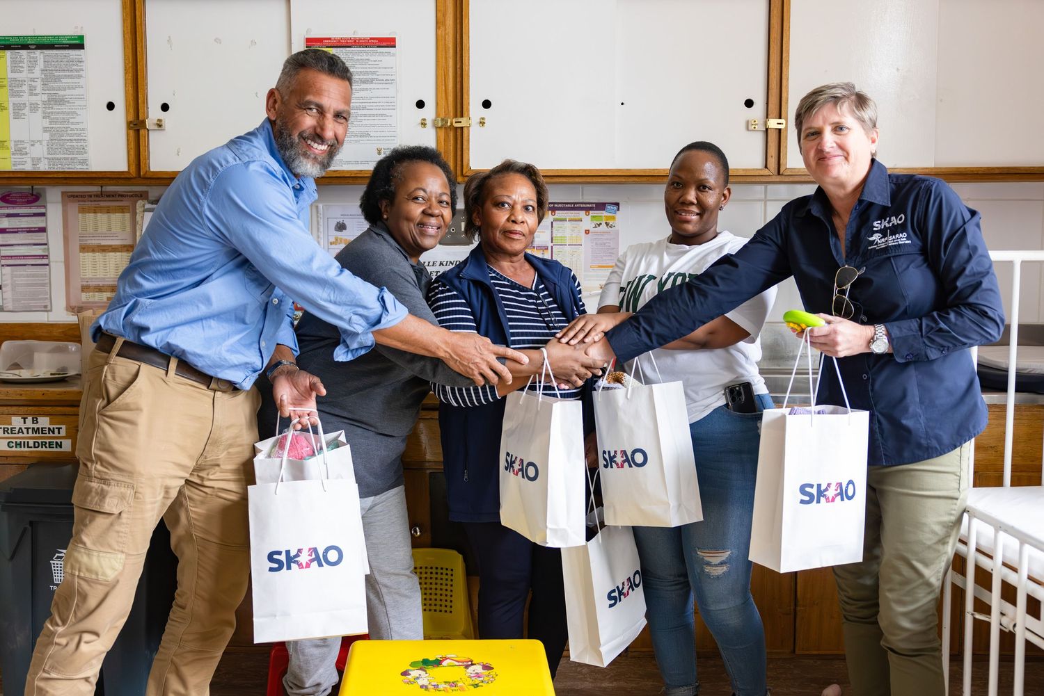 Team members joining hands in celebration while holding branded shopping bags.