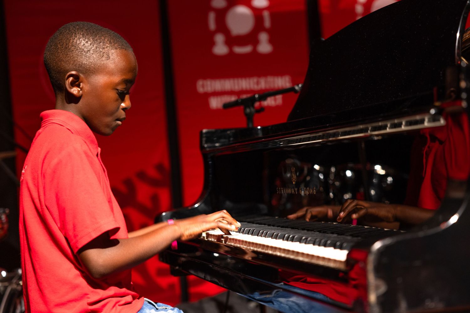 A pianist in a red shirt performs on a grand piano in a dimly lit venue with red lighting.
