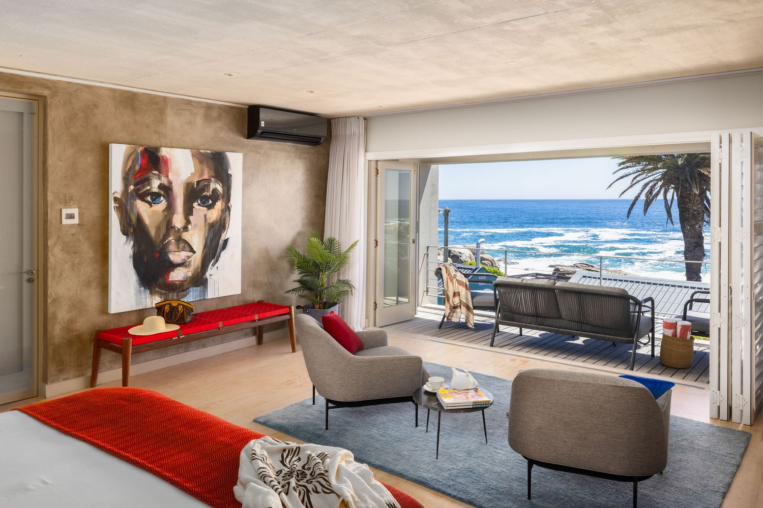 Modern oceanfront condo interior with floor-to-ceiling windows, red accent furniture, and panoramic coastal views.