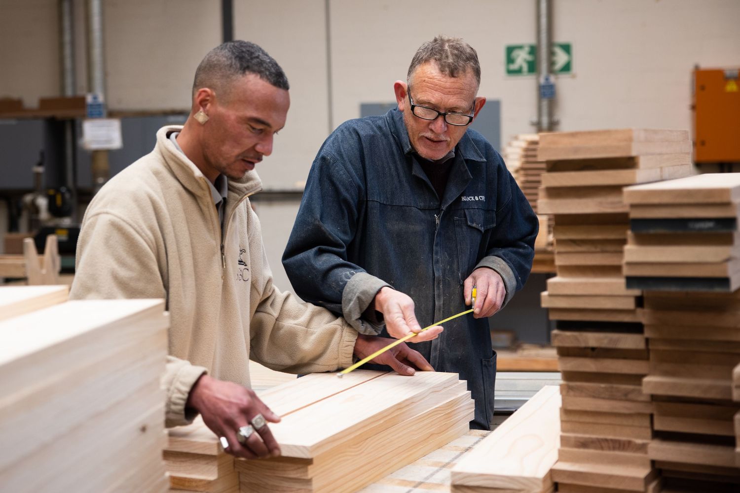 Workers examine wooden components on a manufacturing table.