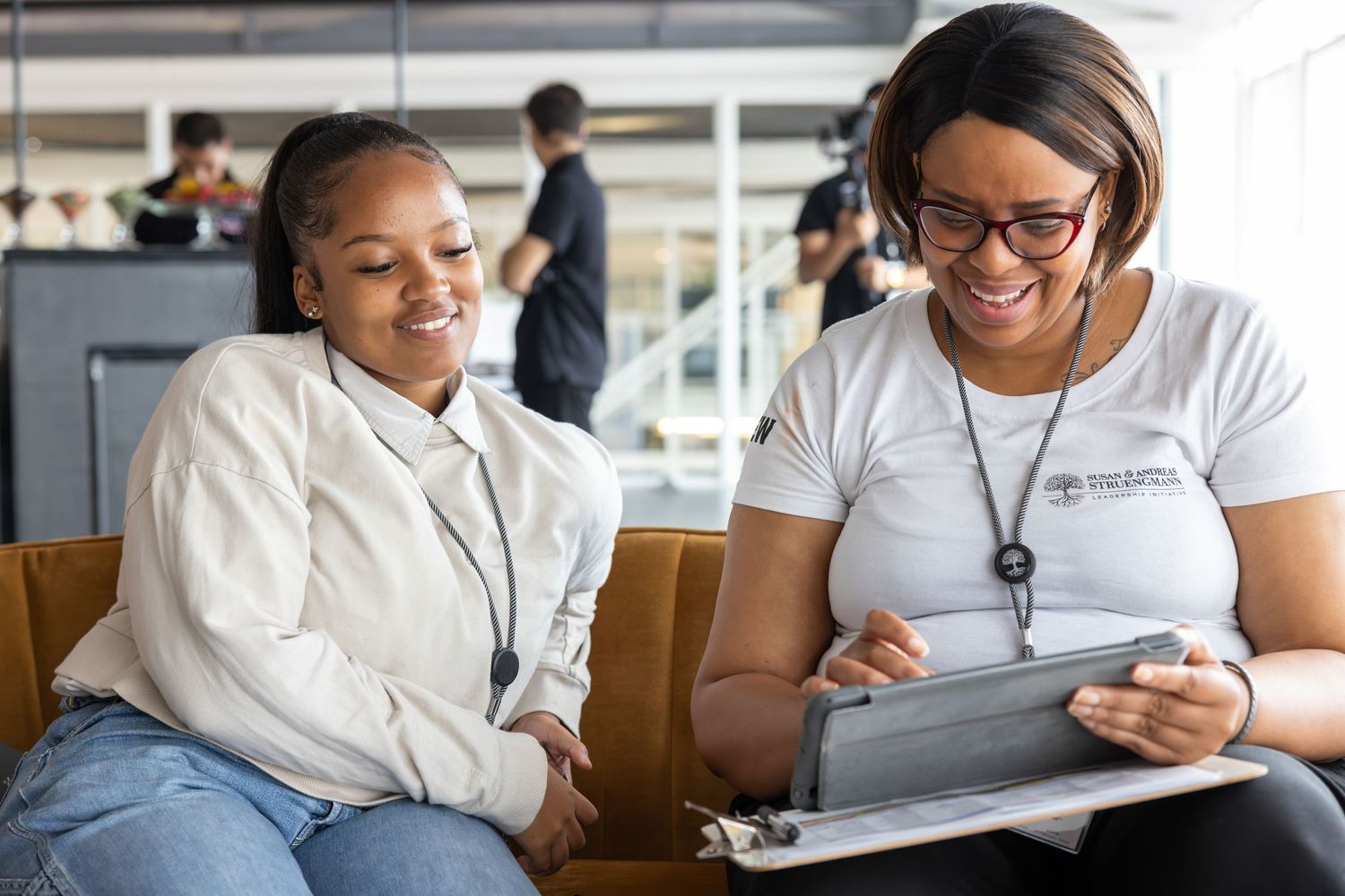 Two students smile while looking at digital content on a tablet device.