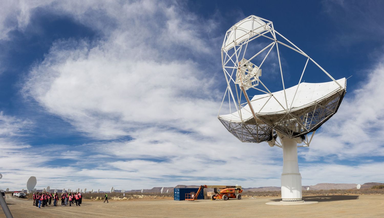 Massive white radio telescope dish installation with vehicles and visitors visible in the desert landscape.