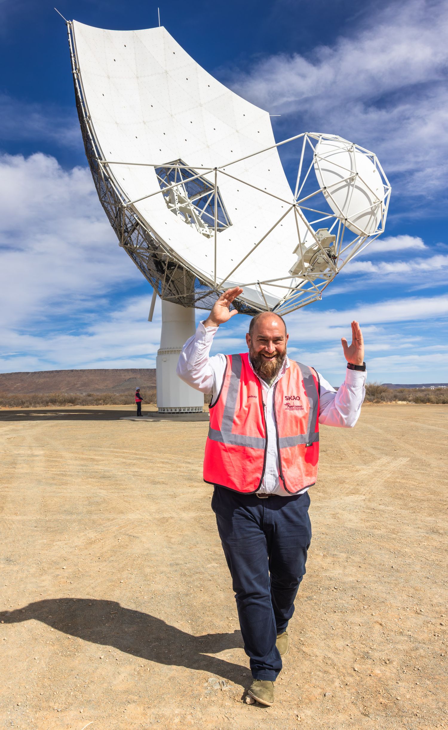 A radio telescope dish installation in a desert landscape against blue skies as a guide gestures enthusiastically.