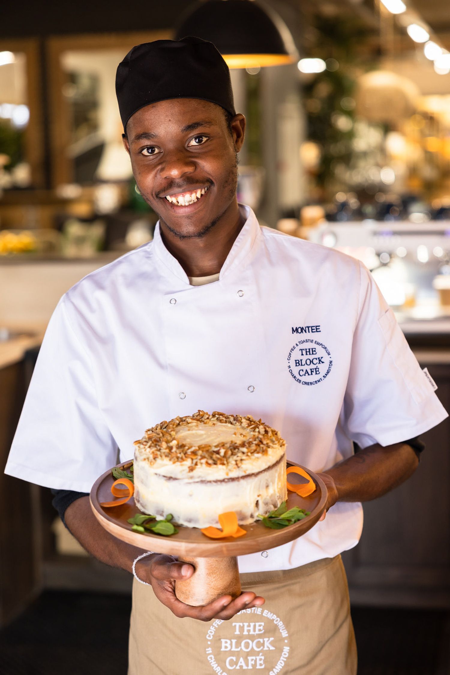 Chef in white uniform presenting a beautifully garnished cake at The Block Cafe.