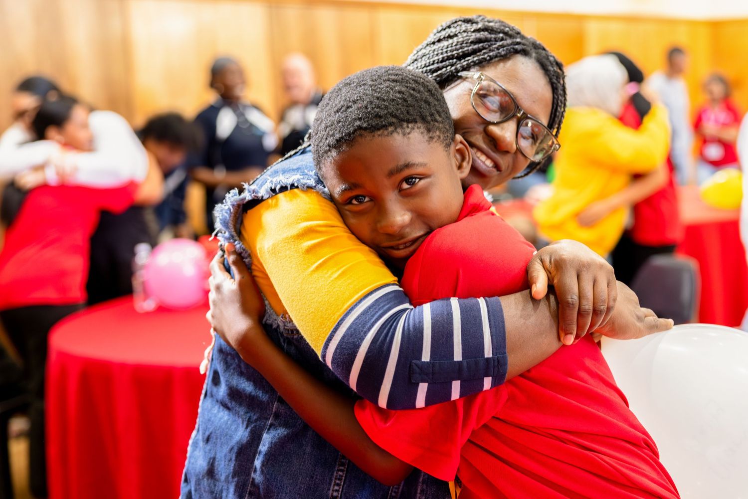 Two participants share a warm embrace during a community event with red decorations.